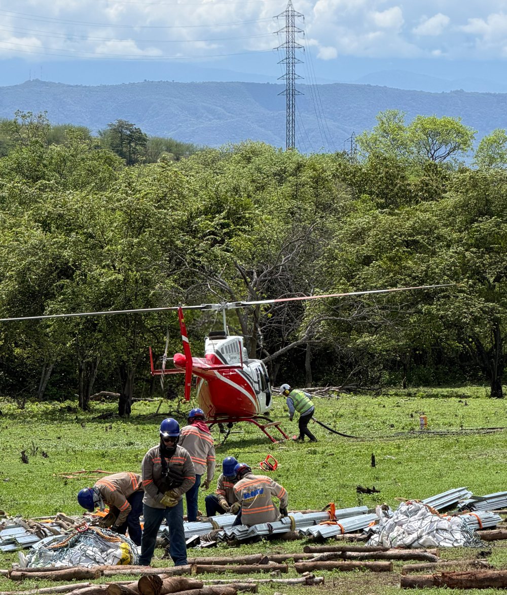 Cuadrilla preparando estructura de torre junto al Bell 206 de Custom, con la línea de transmisión al fondo
